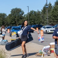 GVSU Alumna poses and GVSU Alumnus carries cardboard box